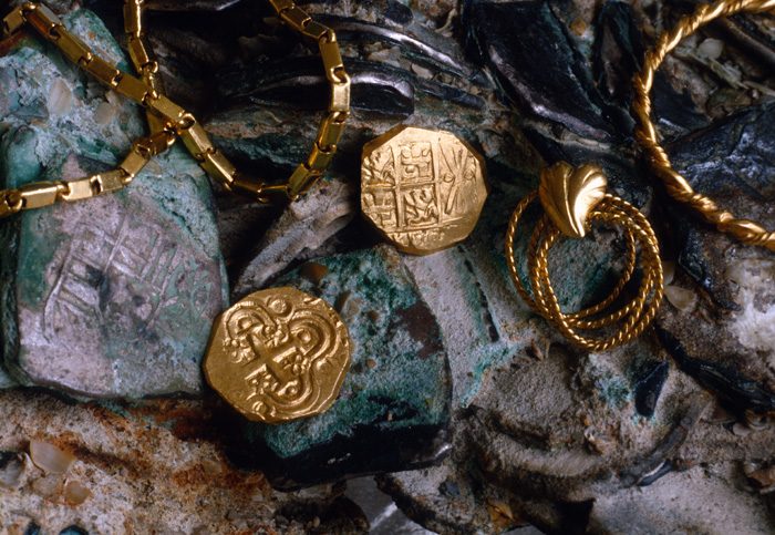 Caption 18- A pair of two escudo gold pieces from the Santa Fé de Bogotá mint, showing both the obverse and reverse of this popular 18th Century gold issue. The escudos rest on a clump of Mexico eight silver reales, whose design is clearly visible below the gold chain at the left. -1715 Fleet
