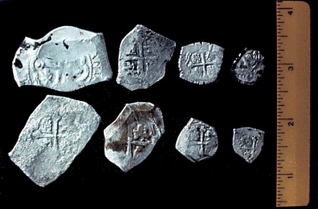 These angular coins look crude compared to the well-minted coins of other eras. Part of their fascination, however, lies in their irregularity. No two coins are alike. Each piece was chiseled from a flat bar of silver then stamped with the royal coat of arms on one side and a cross on the other.  The mark "M" on many coins identifies them of the Mexico City mint. In the home country these cobs were probably to be re-minted into more regular coins. For this reason and because of shipwreck and the scarcity of transport during the War of Spanish Succession, museums and collectors own few examples of New World cobs from the 1700-1715 period.
